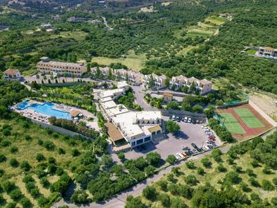 Aerial view of a resort with a pool, tennis court, surrounded by greenery and hills.