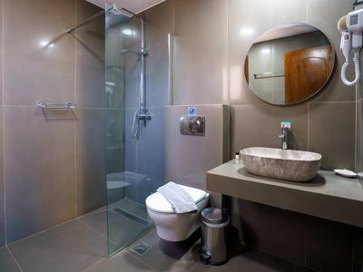Modern hotel bathroom with glass shower, round mirror, and gray tiles.