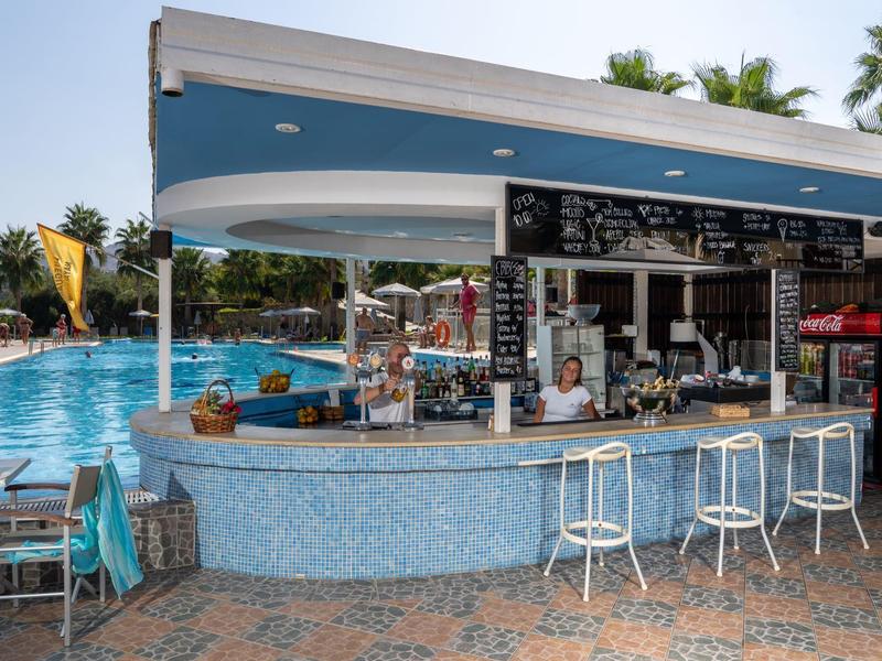 Round pool bar with stools next to a swimming pool under a clear sky.
