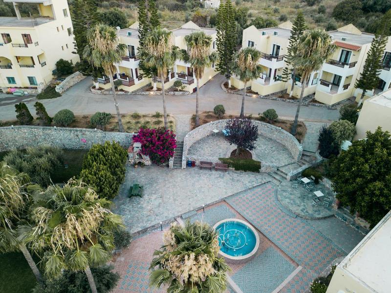 Top view of a hotel pool area with palm trees and white buildings.