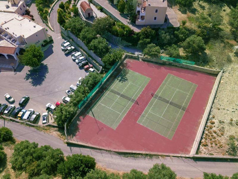 Aerial view of two tennis courts next to a parking lot and green trees.