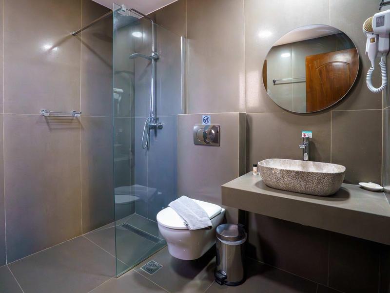 Modern hotel bathroom with glass shower, round mirror, and gray tiles.