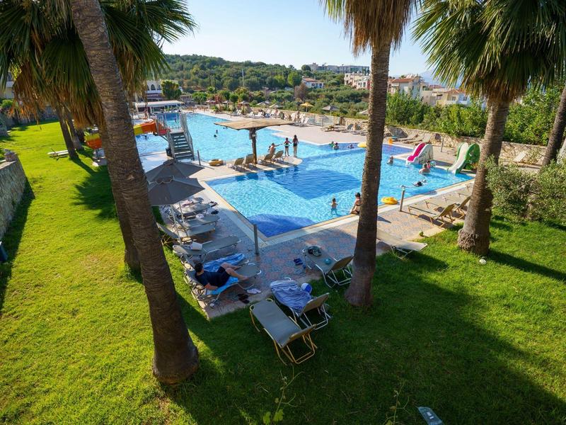 Pool area with sun loungers and palm trees in a sunny hotel resort.