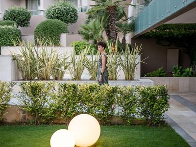 Frau geht neben üppigem Grün und Lampen im Außenbereich eines Hotels spazieren.