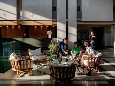 Hotel-Lounge mit Gästen, die auf Sesseln um einen Glastisch sitzen und sich unterhalten.