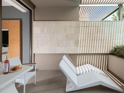 Balcón moderno con tumbona, mesa con vino y aperitivos, panel decorativo y plantas.