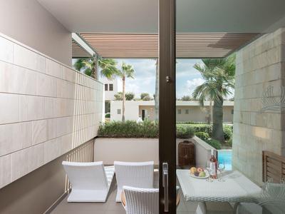 Balcón con mesa, sillas y vista a un jardín con palmeras y edificios al fondo.