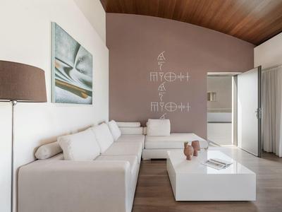 Sala de estar luminosa con sofá en esquina blanco y arte abstracto en la pared en una habitación de hotel.