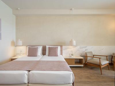 Habitación de hotel moderna con cama doble, dos almohadas, luces nocturnas y un sillón junto a la ventana.