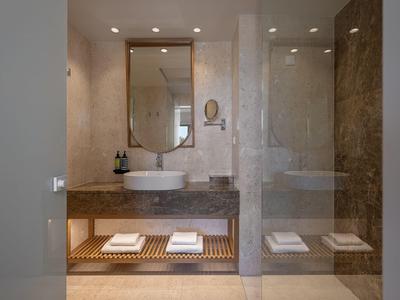 Baño moderno de hotel con lavabo, espejo y toallas sobre un estante de madera.