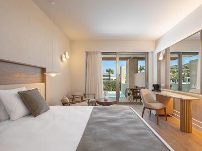 Habitación de hotel luminosa con cama grande, escritorio, silla y terraza con vista a la piscina.