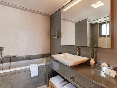 Baño moderno de hotel con bañera, gran espejo y lavabo sobre amplia encimera.