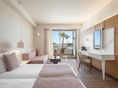 Habitación de hotel luminosa con cama doble, sofá, escritorio y balcón con vista al mar.