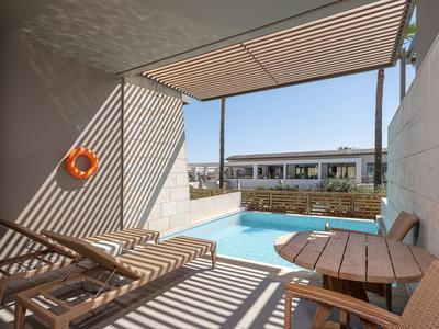 Área de descanso con sombra con tumbonas y piscina pequeña, entorno moderno de hotel.