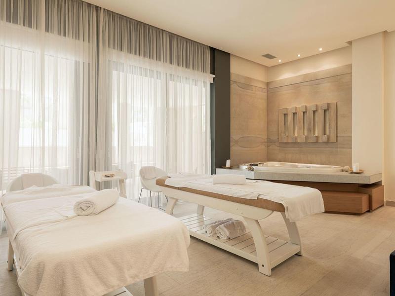 Sala de spa moderna y luminosa con dos camillas de masaje y detalles cálidos de madera.