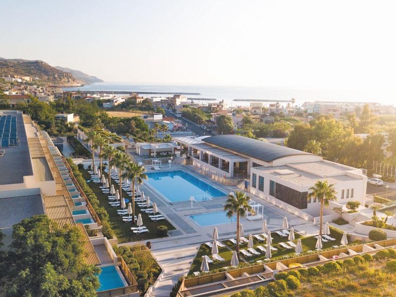 Vista aérea de un hotel con piscinas, terrazas y paisaje circundante al atardecer.