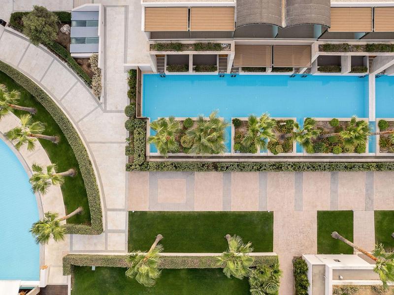 Vista aérea de un hotel con piscina rectangular, plantas verdes y macizos de flores.
