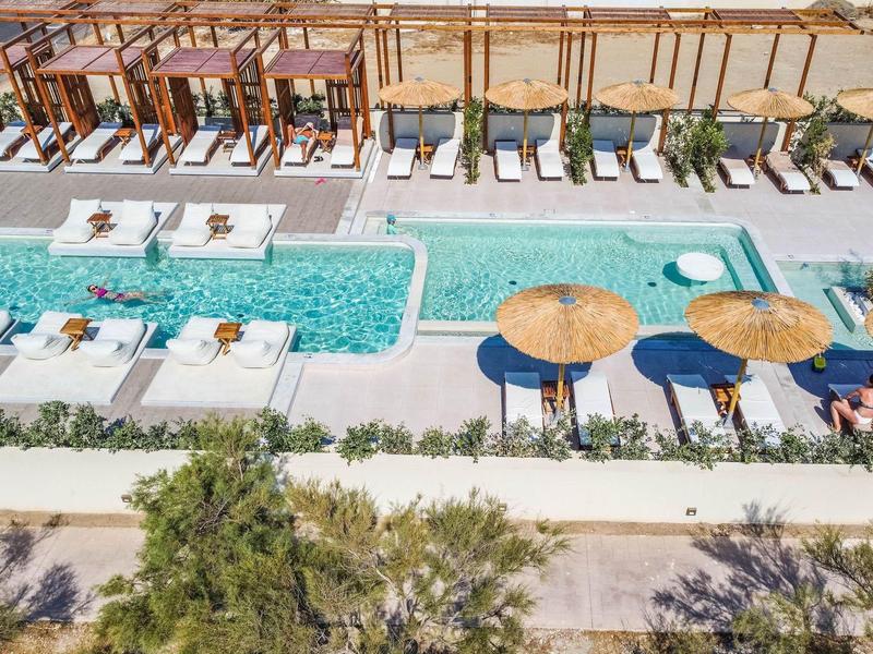 Piscina exterior moderna con tumbonas, sombrillas y áreas de descanso junto a un hotel.