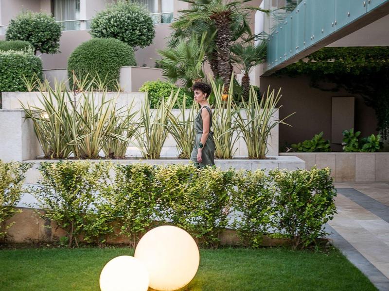 Mujer camina junto a arbustos y plantas verdes en un jardín del hotel.
