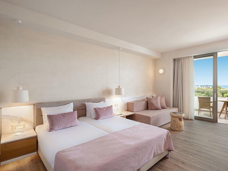 Habitat hotelero luminoso con cama doble, sofá, balcón y vista al mar.