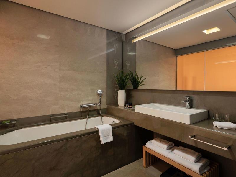Baño moderno con bañera empotrada, lavabo amplio y espejo grande con plantas decorativas.