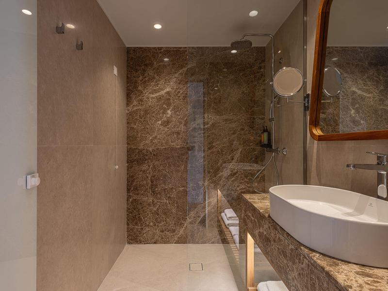 Baño de hotel moderno con pared lisa, ducha de vidrio grande y amplio lavabo con espejo.