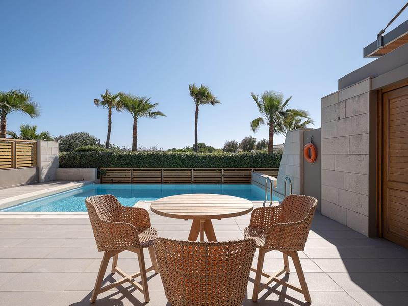 Piscina exterior moderna con palmeras y sillas de mimbre alrededor de una mesa redonda.