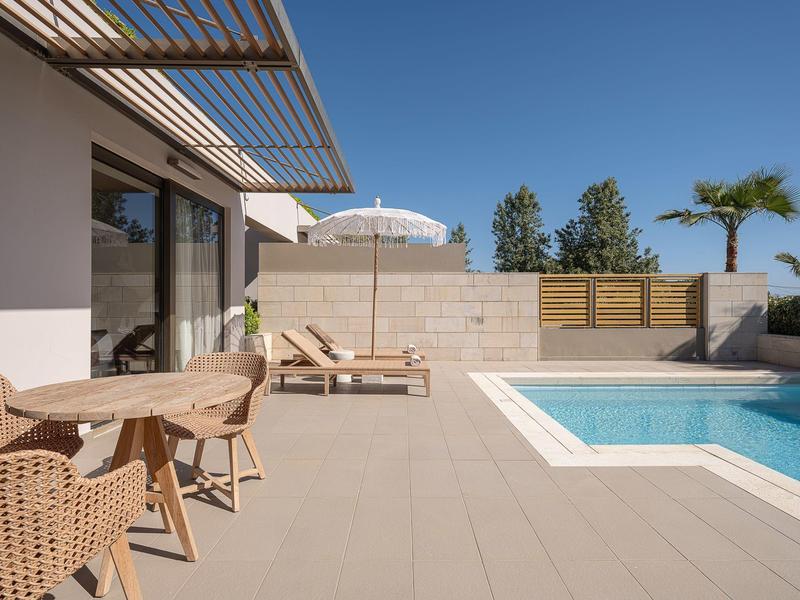 Área exterior moderna con piscina, tumbonas, sombrilla y zona de estar bajo cielo despejado.