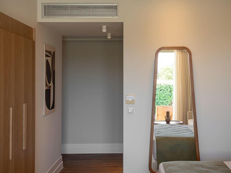 Habitación sencilla con un pequeño armario, espejo y una cama individual junto a la pared.