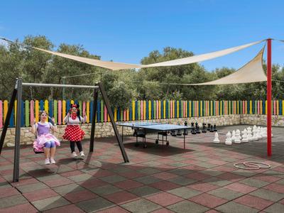 Área de juegos con dos niños en columpios, mesa de ping-pong y velas de sombra al aire libre.
