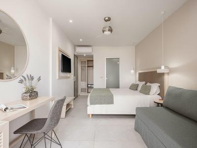 Habitación de hotel moderna equipada con cama doble, sofá, TV de pantalla plana y espejo decorativo.