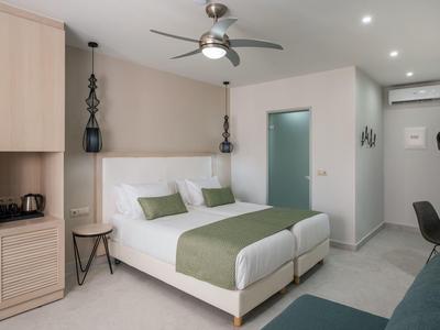 Habitación de hotel luminosa con dos camas individuales, ventilador de techo y mobiliario moderno.