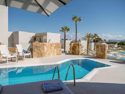 Piscina al aire libre moderna con tumbonas y sombrilla, rodeada de palmeras y montañas.