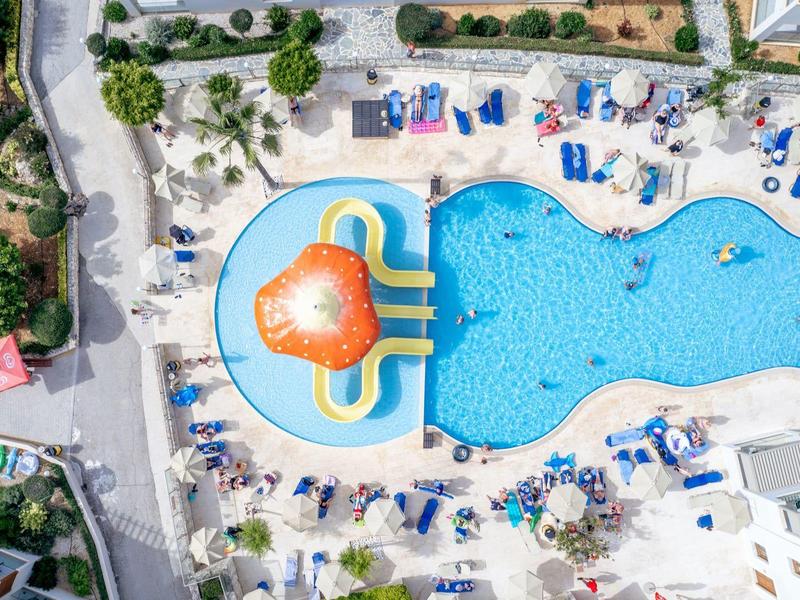 Vista aérea de un hotel con piscina grande y tobogán acuático en área con forma de corazón.