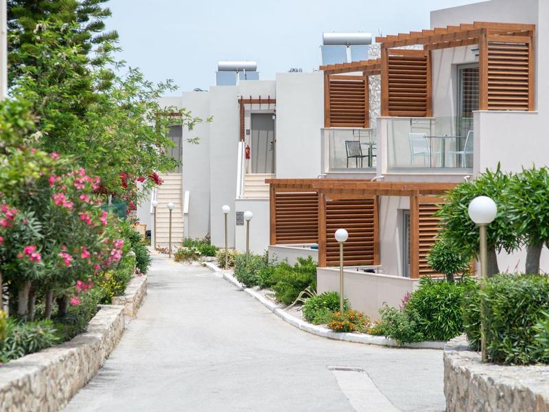 Complejo hotelero moderno con fachada blanca, revestimiento de madera y vegetación verde a lo largo de un sendero.
