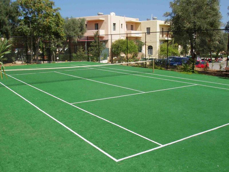 Cancha de tenis verde con líneas blancas junto a un edificio de hotel y árboles.