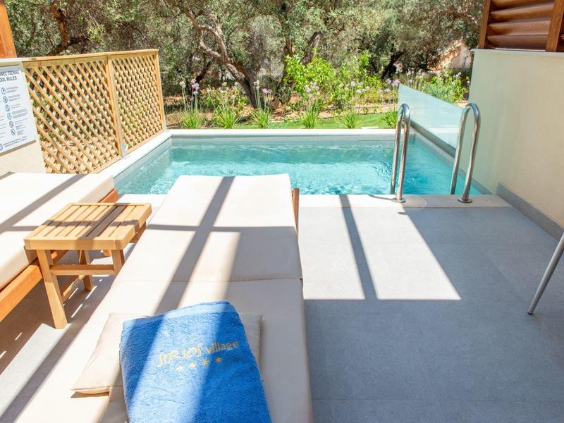 Área de piscina pequeña con toalla azul, tumbonas y árboles al fondo en un entorno soleado.