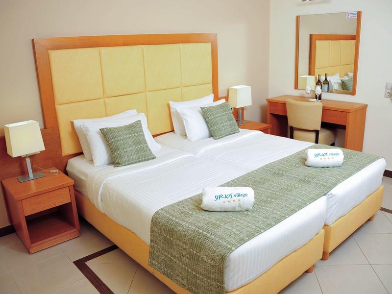 Habitación con dos camas individuales, cobertores verdes, mesitas de noche y tocador con espejo.