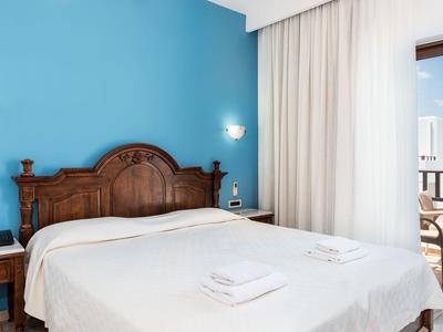 Jasny pokój hotelowy z dużym drewnianym łóżkiem i balkonem.