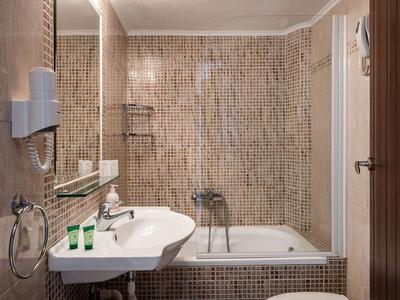 Salle de bain moderne avec carrelage en mosaïque, baignoire, lavabo et sèche-cheveux.