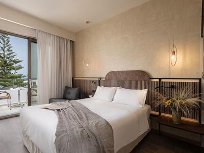 Chambre d'hôtel lumineuse avec grand lit, balcon et vue sur les arbres.