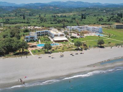 Kompleks hotelowy z basenem blisko plaży i gór w tle.