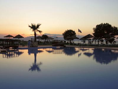 Basen o zachodzie słońca z palmami i parasolami odbijającymi się w wodzie.