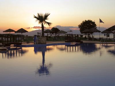 Schwimmbad mit Palmbaum und Sonnenschirmen bei Sonnenuntergang