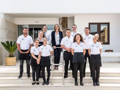 Hotelpersonal in einheitlicher Kleidung steht vor einem weißen Gebäude mit Stufen.