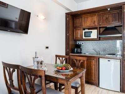 Jadalnia z drewnianym stołem, krzesłami i małym aneksem kuchennym z lodówką i mikrofalówką.