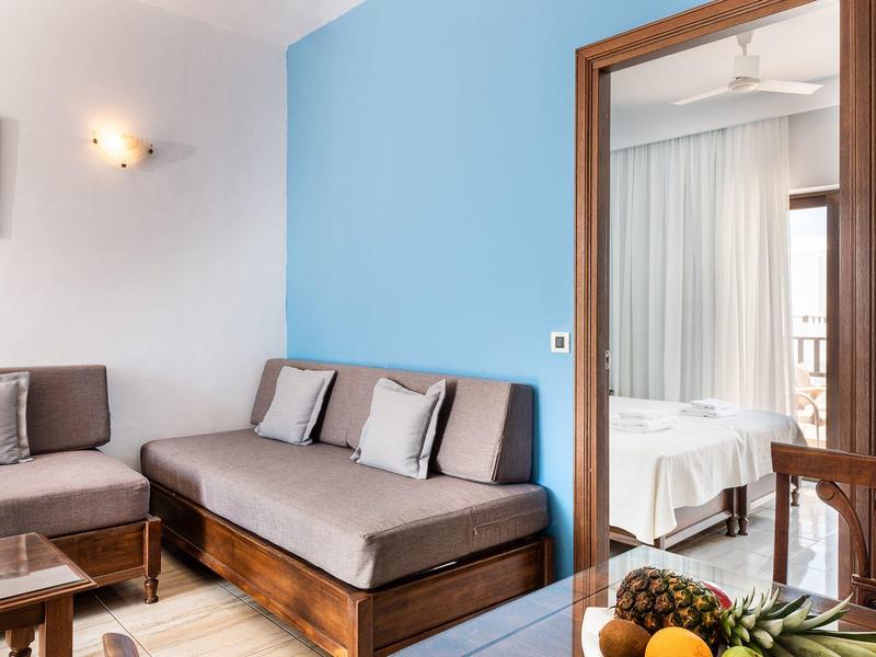 Przytulny salon z brązową kanapą, szarymi poduszkami i widokiem na sypialnię.