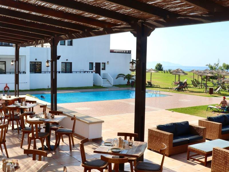 Zadaszony taras na zewnątrz z drewnianymi stolikami i krzesłami obok basenu z widokiem na morze.