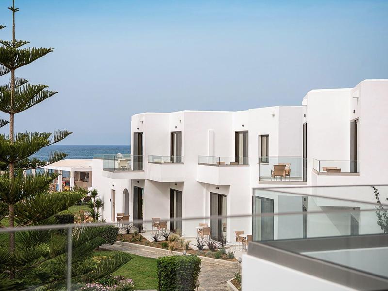 Białe nowoczesne budynki hotelowe blisko morza, z jasnym niebem i zielenią.
