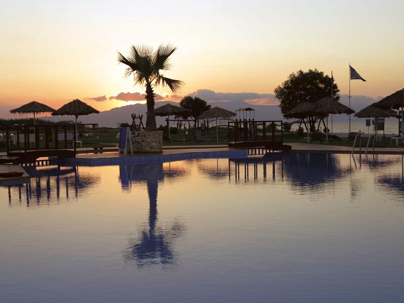 Basen o zachodzie słońca z palmami i parasolami nad wodą.